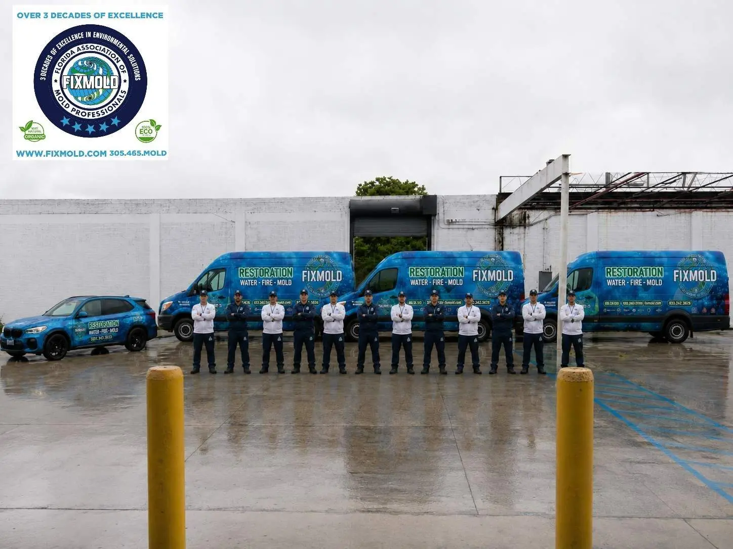 Line of blue Fixmold restoration vans and a crew standing in a wet parking lot beside a white wall; top-left shows an organization logo.